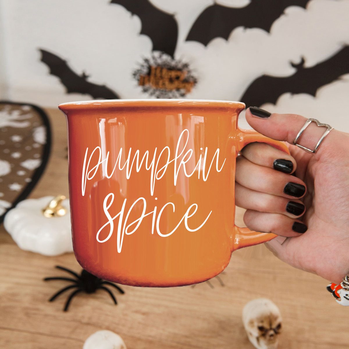 Orange ceramic mug with white pumpkin spice lettering, held by a ringed hand