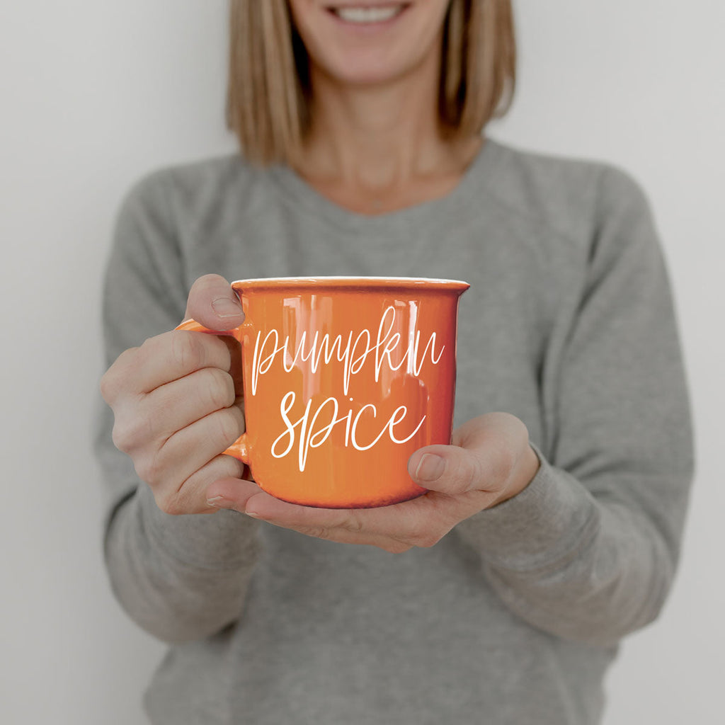 Orange ceramic mug with 'Pumpkin Spice' text, held toward camera