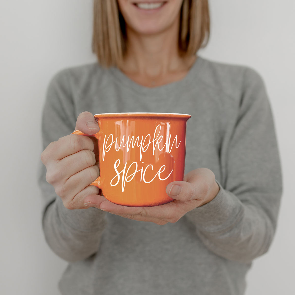 Orange ceramic mug with 'Pumpkin Spice' text, held toward camera