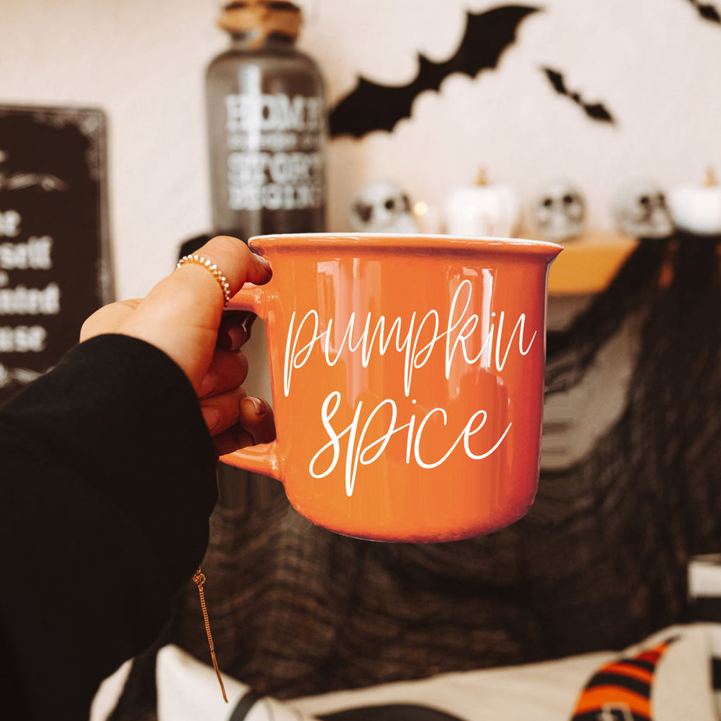 Orange ceramic mug with white “pumpkin spice” script lettering held in hand