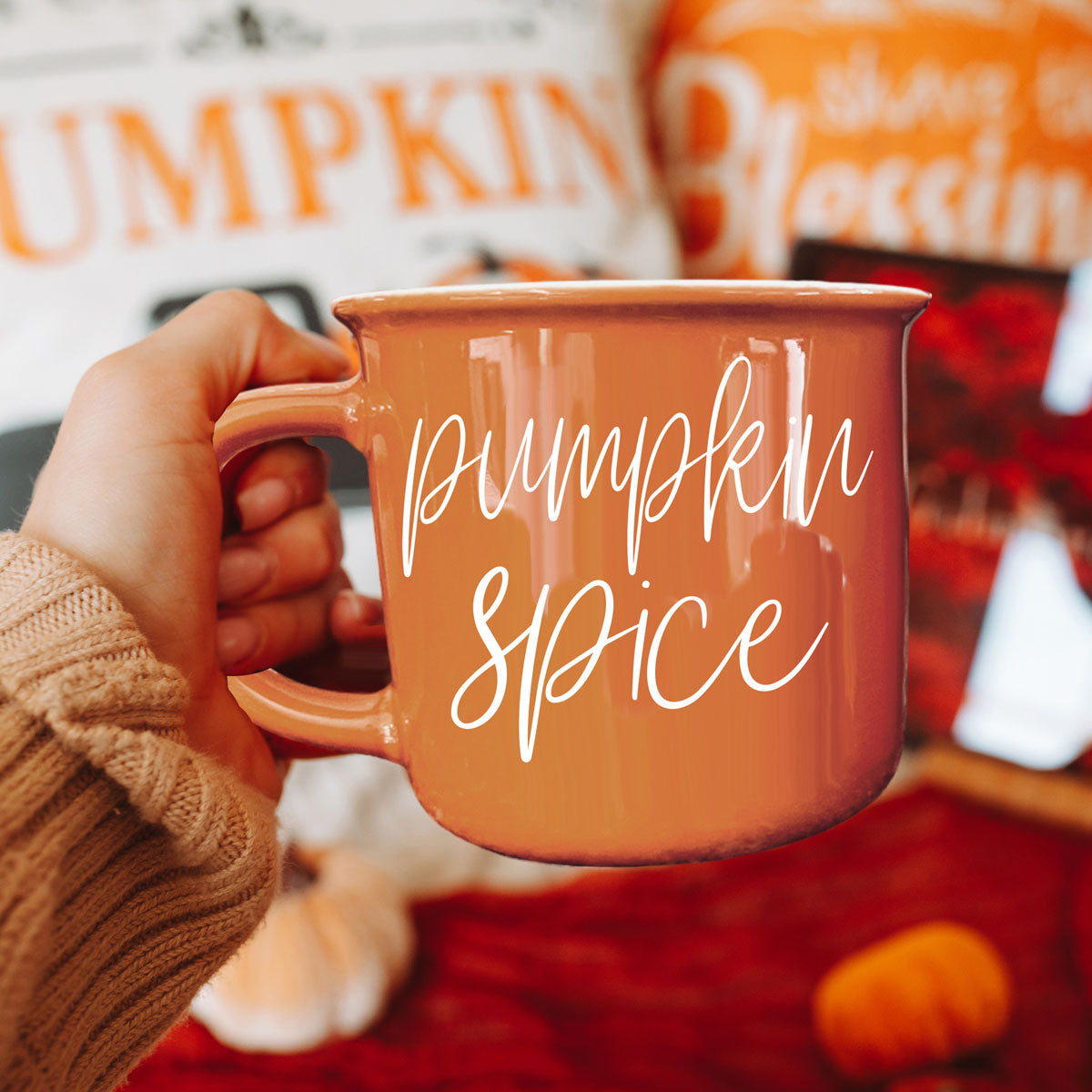 Orange ceramic coffee mug with white pumpkin spice script, held in a hand