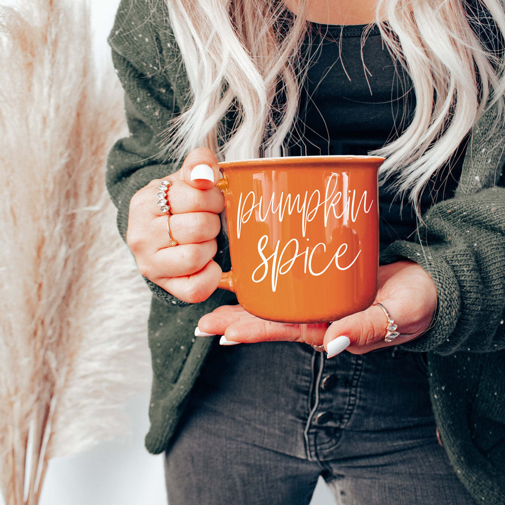 Orange ceramic mug with white pumpkin spice lettering, held by person in dark sweater