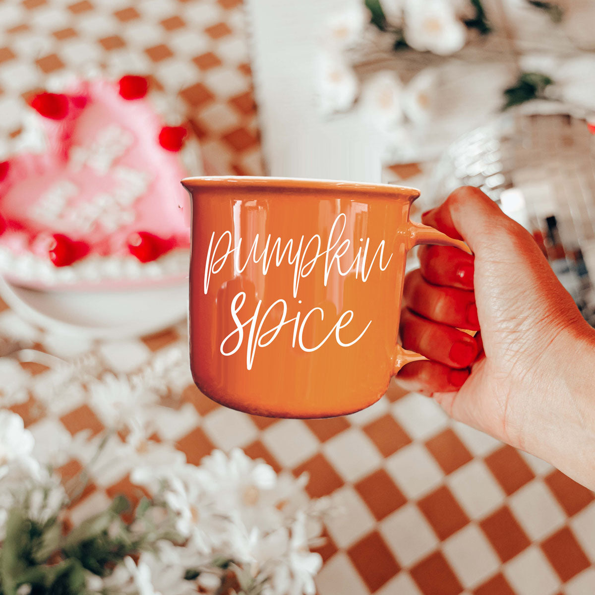 Orange mug with white cursive pumpkin spice text, held up by a hand