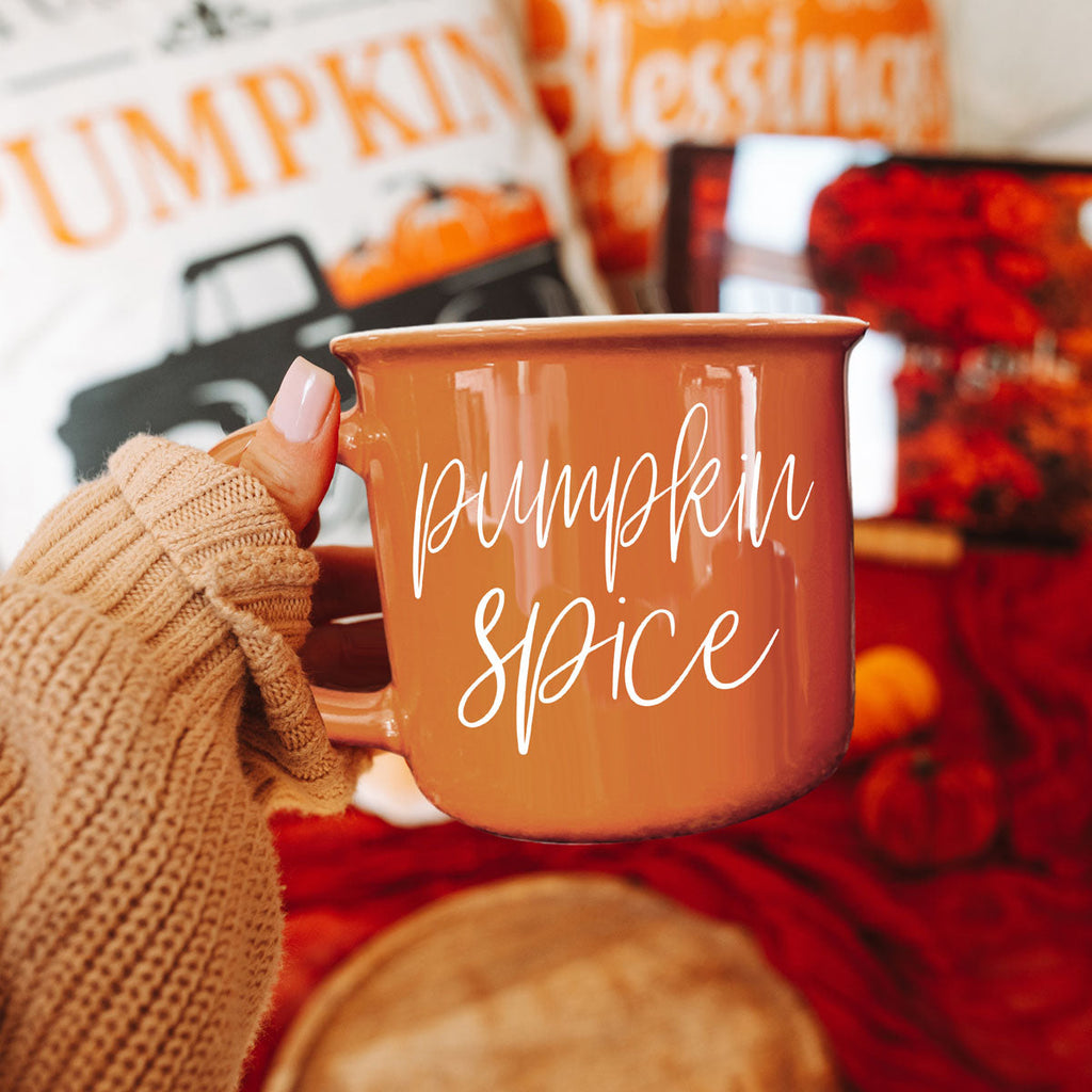 Orange ceramic mug with white pumpkin spice script, gripped by a knit sleeve