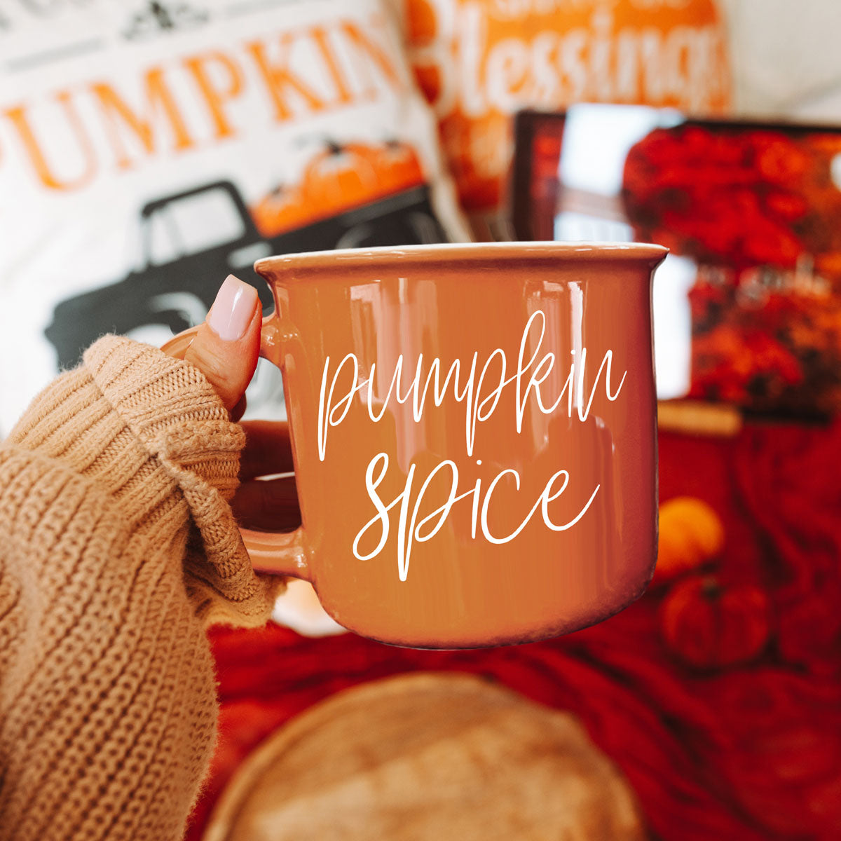 Orange ceramic mug with white pumpkin spice script, gripped by a knit sleeve