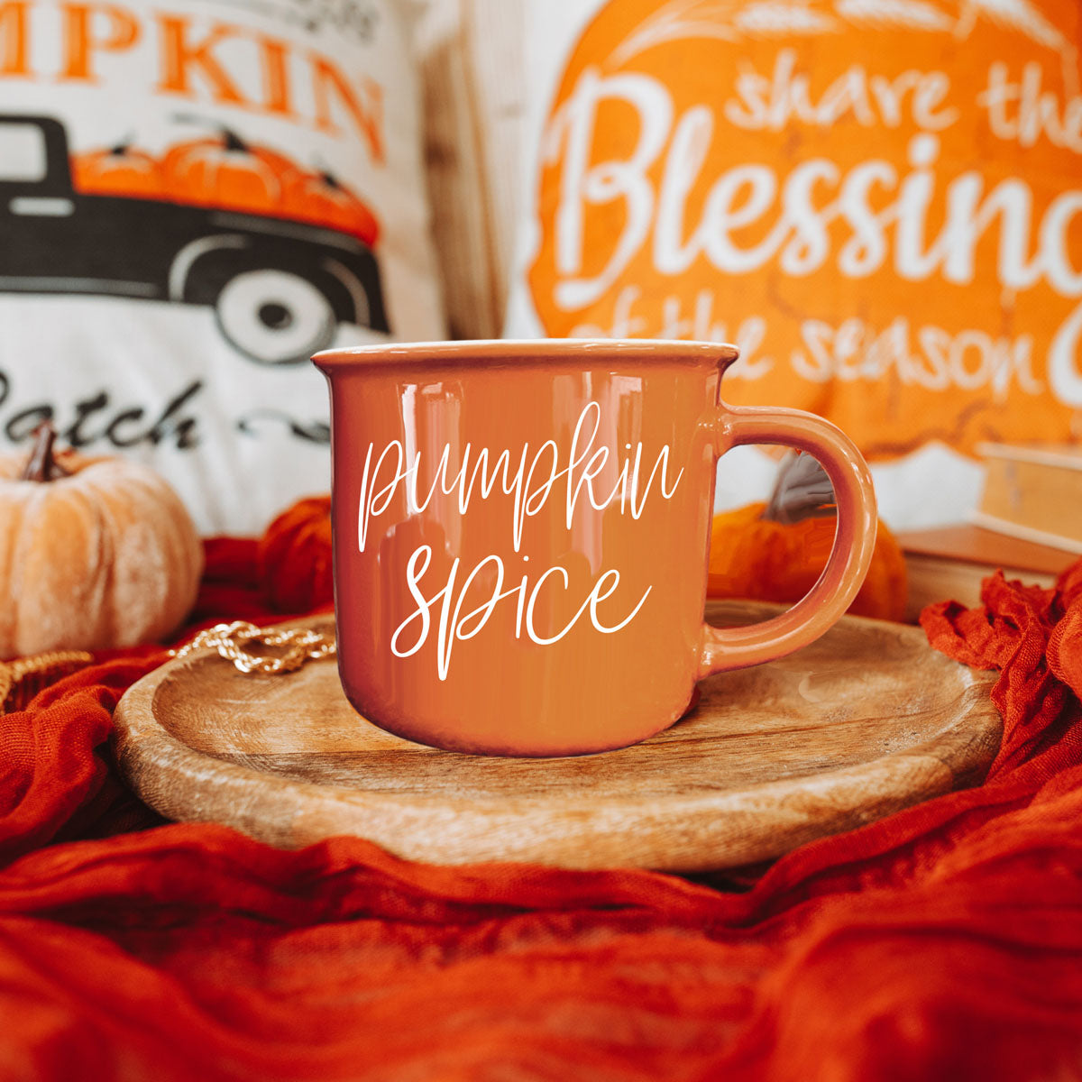 Orange ceramic mug with white cursive pumpkin spice text, shown on a round tray