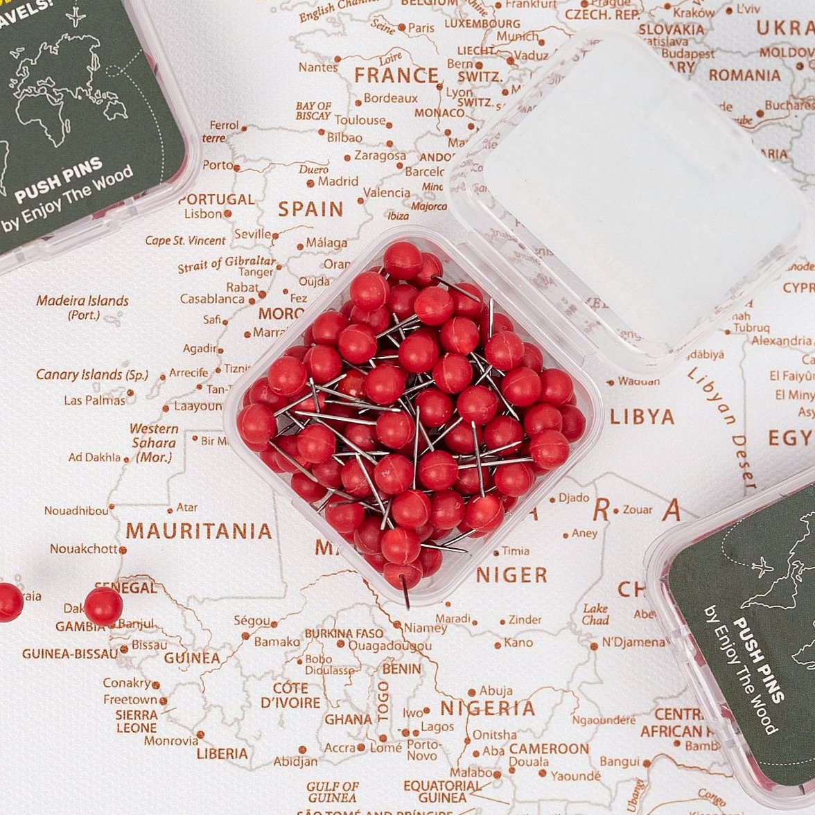 Red round push pins scattered in a clear tray on a canvas world map