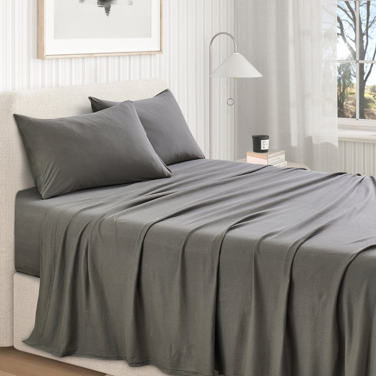 Grey jersey knit sheet set on bed with two pillowcases and flat sheet drape