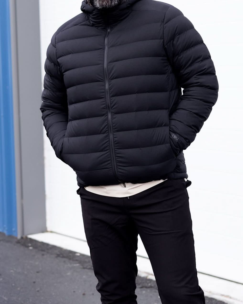 Black puffer down jacket with hood, full-zip front, and side profile stitching detail