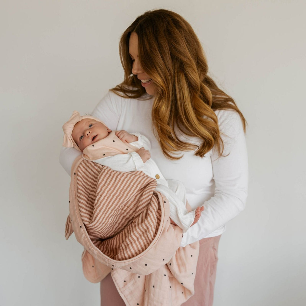 Blush muslin quilt wrapped on baby with striped layer