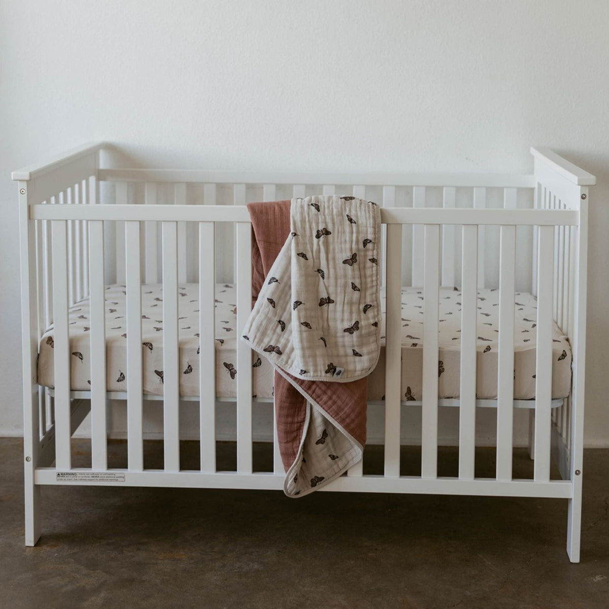 Butterfly quilt draped on a white crib, beige muslin with dark butterfly print