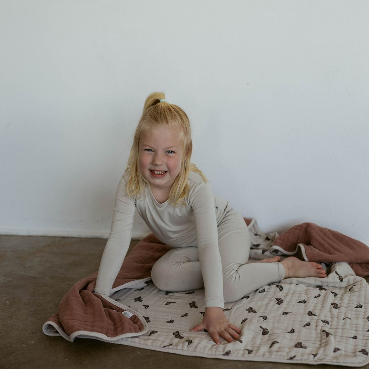 Child lying on the floor with a beige quilt featuring dark butterfly print and terracotta trim