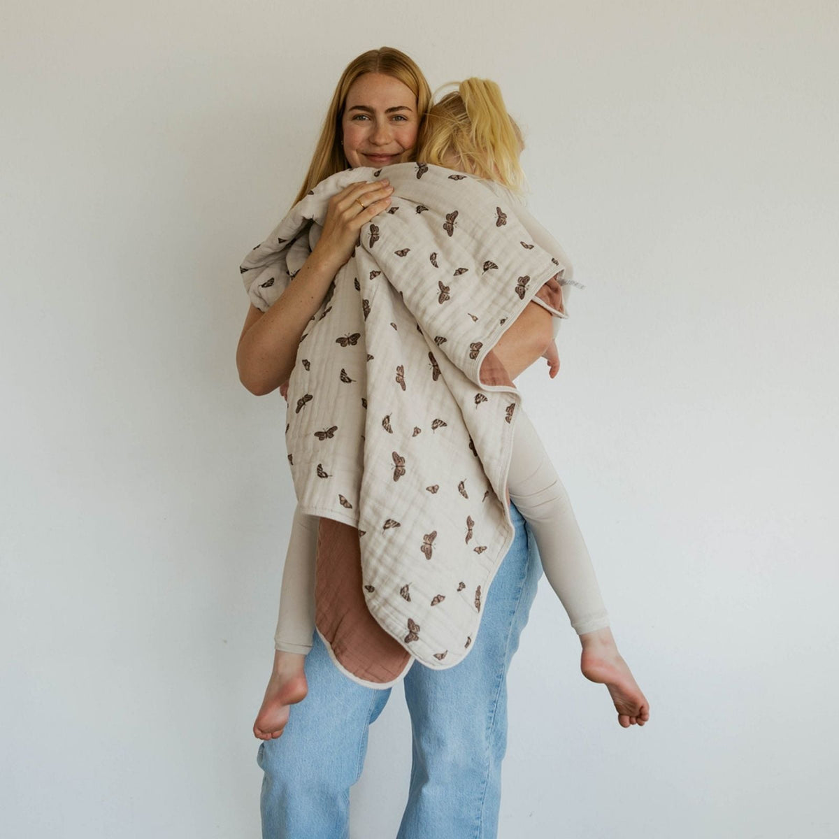 Muslin quilt wrap on a person, beige with dark butterfly print and terracotta underside