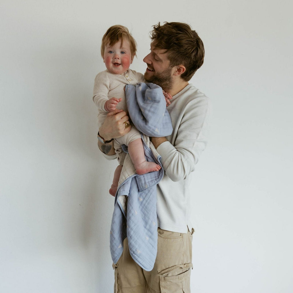 Light blue cloud-pattern muslin quilt draped over toddler and parent
