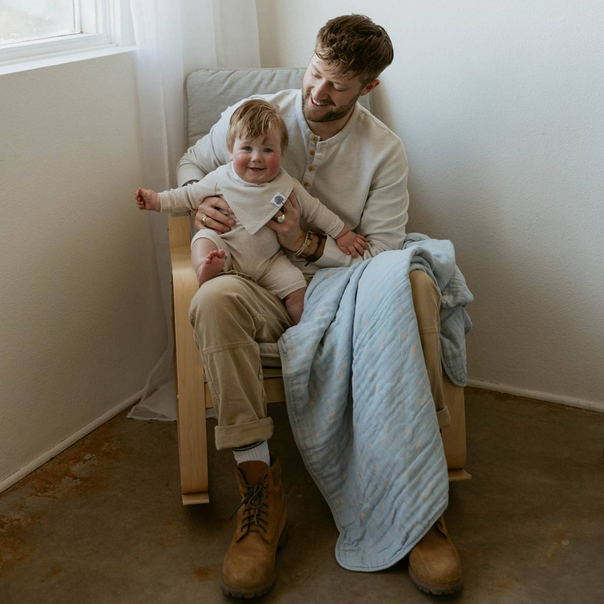 Light blue muslin quilt draped over child on wooden rocking chair
