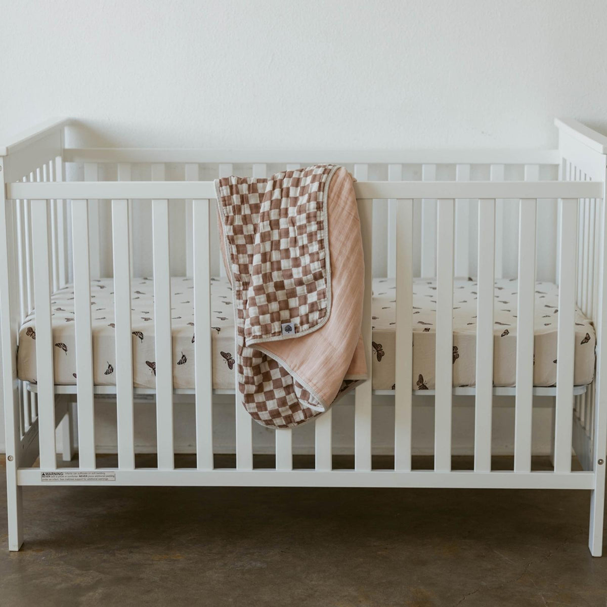 Rosewood checker-pattern quilt draped over a baby crib rail