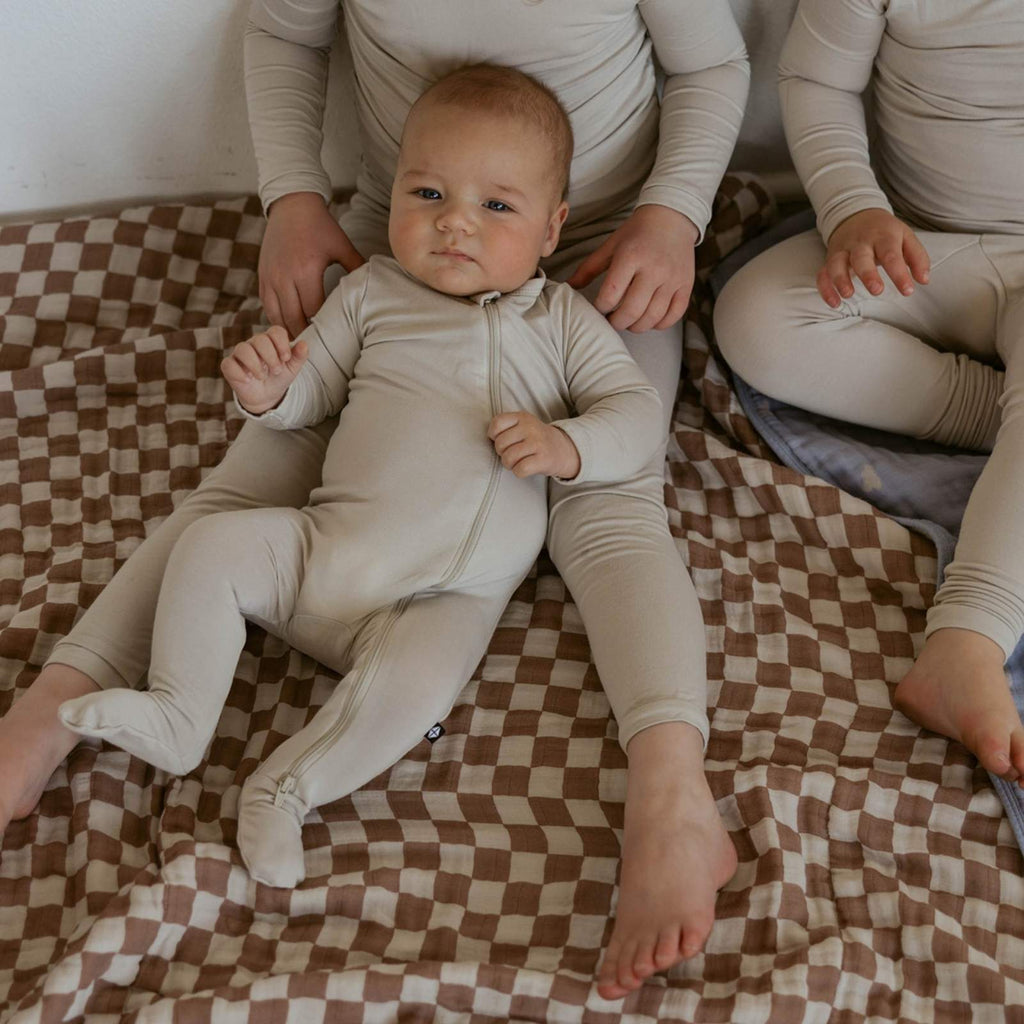 Baby lying on a rosewood checker-pattern quilt with pink-edged panel