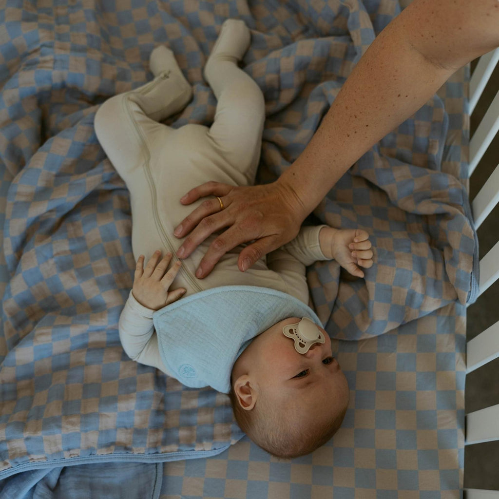 Blue-and-tan checker muslin quilt under baby while held by caregiver