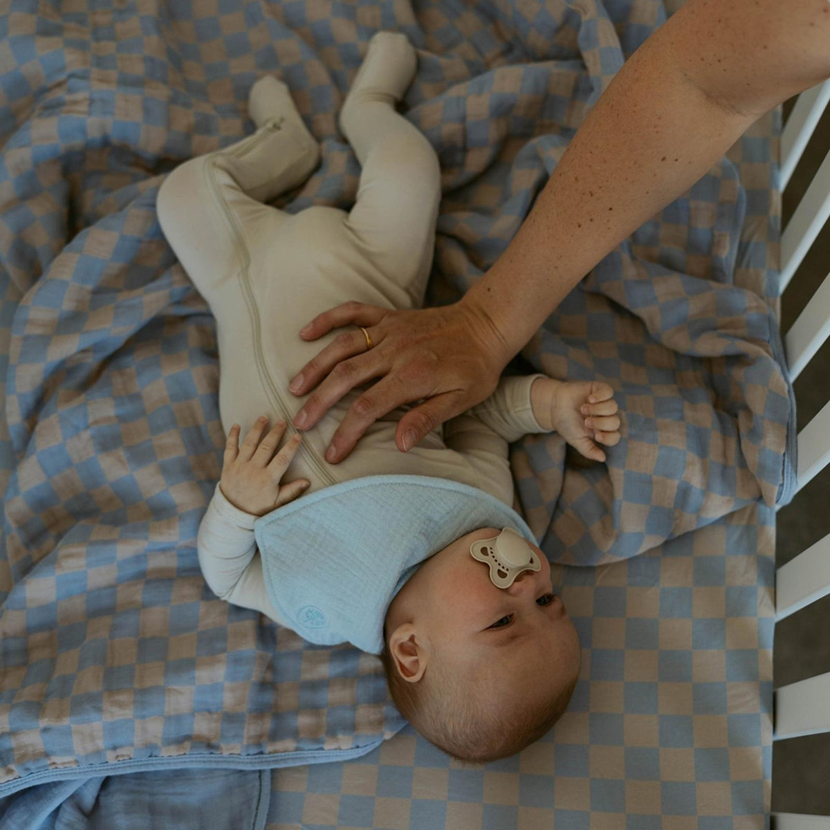 Blue-and-tan checker muslin quilt under baby while held by caregiver