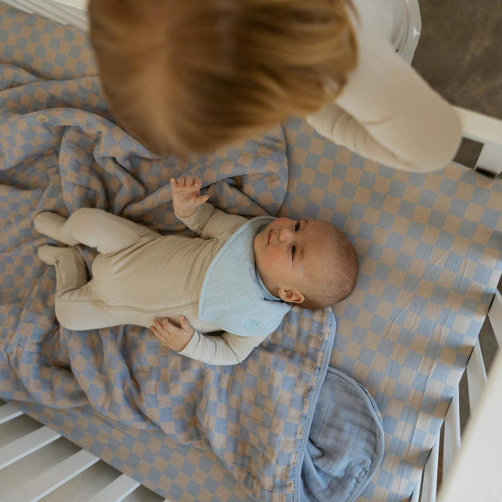 Baby lying on blue-and-tan check muslin quilt in a nursery
