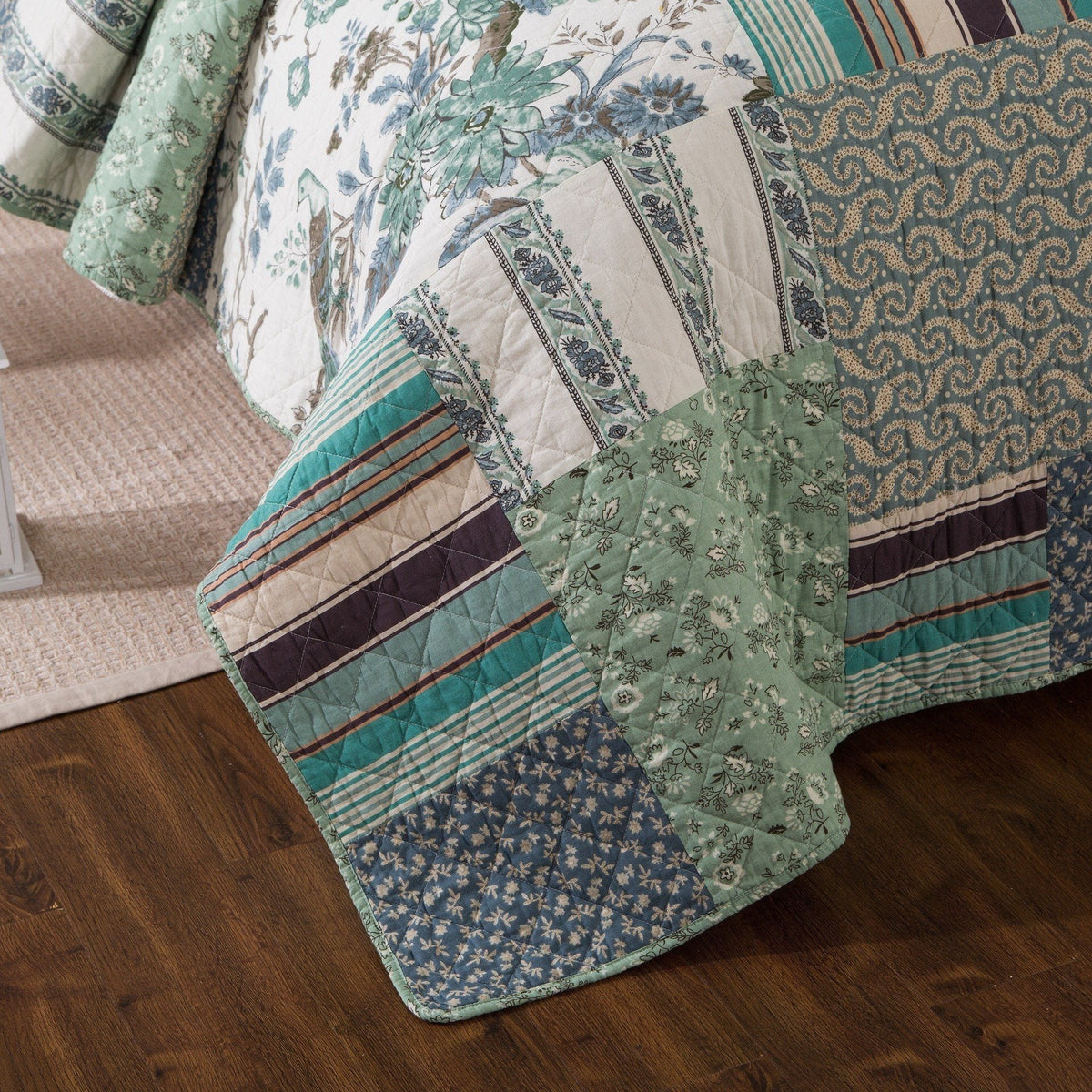Quilted bedspread corner with floral and stripe patchwork in teal, green, and navy