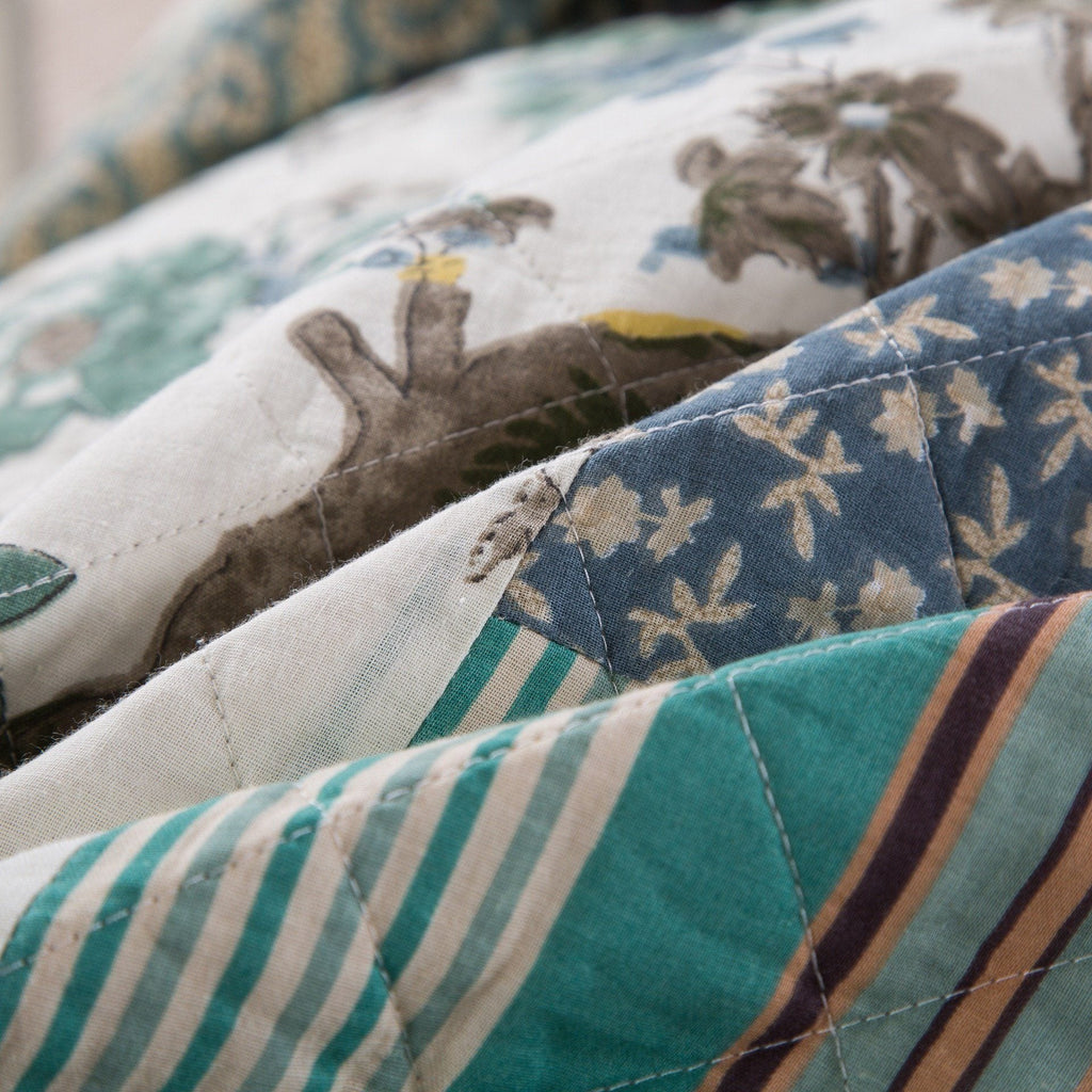 Close-up quilt stitching on bedspread with teal, navy, and beige patchwork stripes