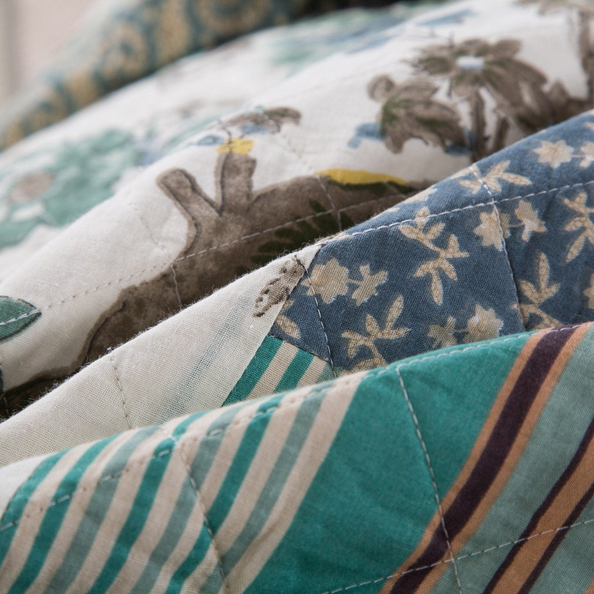 Close-up quilt stitching on bedspread with teal, navy, and beige patchwork stripes