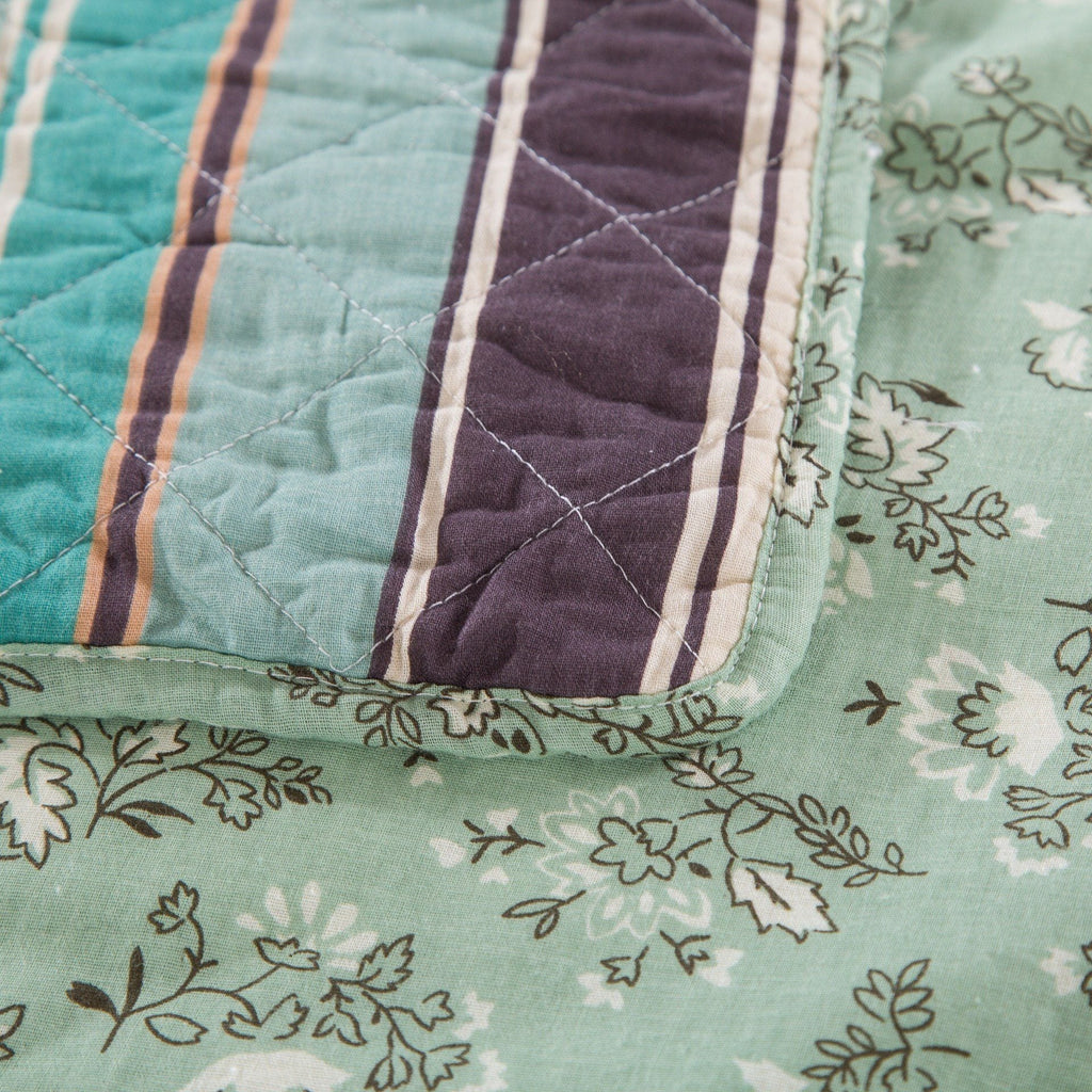 Quilted bedspread fabric corner with stitched panels in teal, plum, and cream