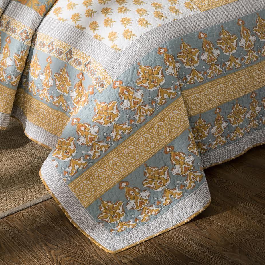 Cotton quilt bedspread corner detail with light blue stripes and gold floral trim