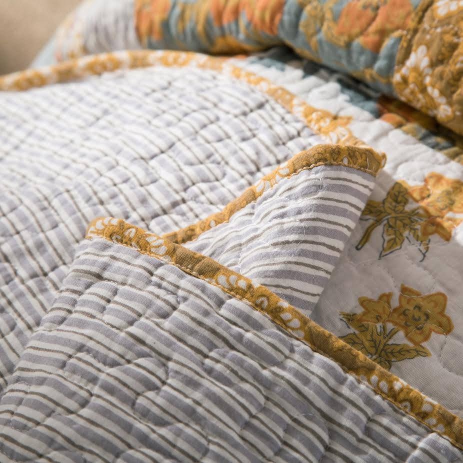 Cotton quilt bedspread close-up showing quilted stripes, floral accents, and gold edging