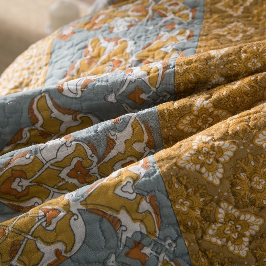Cotton quilt bedspread fabric close-up with blue horse motifs and gold floral blocks
