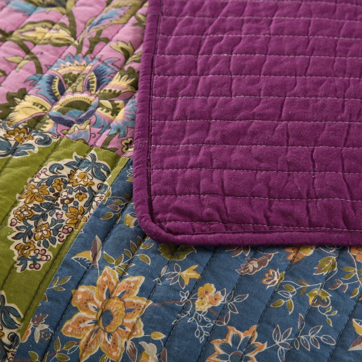 Quilted bedspread corner with deep purple border and floral patchwork panel