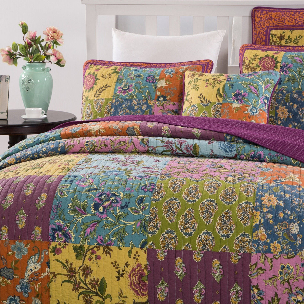 Quilted bedspread and pillow shams in vibrant floral patchwork with purple trim
