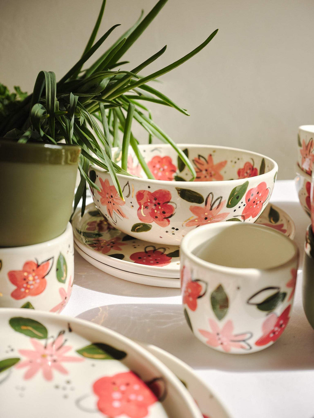 Porcelain salad bowls and cups with hand-painted pink floral motifs, stacked on table