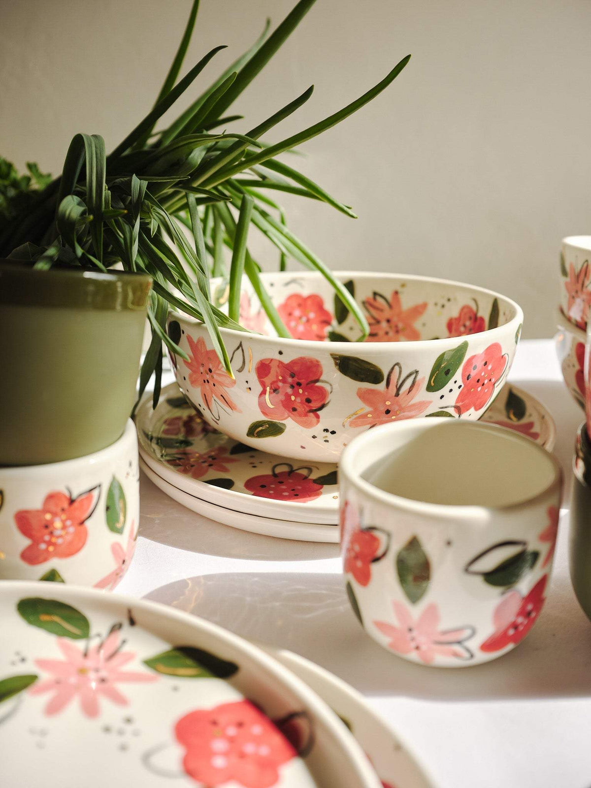 Porcelain salad bowls and cups with hand-painted pink floral motifs, stacked on table