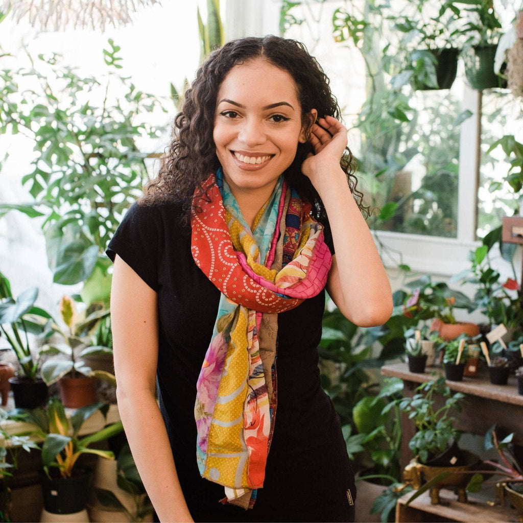 Orange and teal patchwork scarf with yellow and purple floral motifs worn by woman.