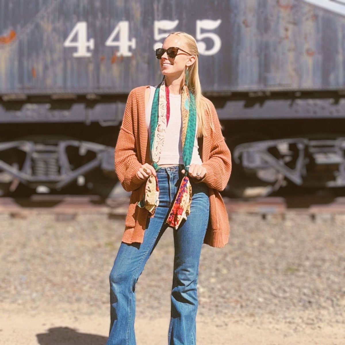 Multicolor patchwork scarf draped over jeans with teal, green, and red stripes.