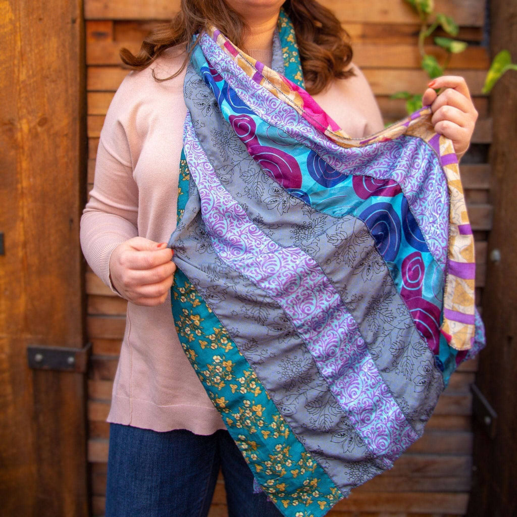 Woman holding a multicolor patchwork scarf with purple, blue, and gold border stripes.