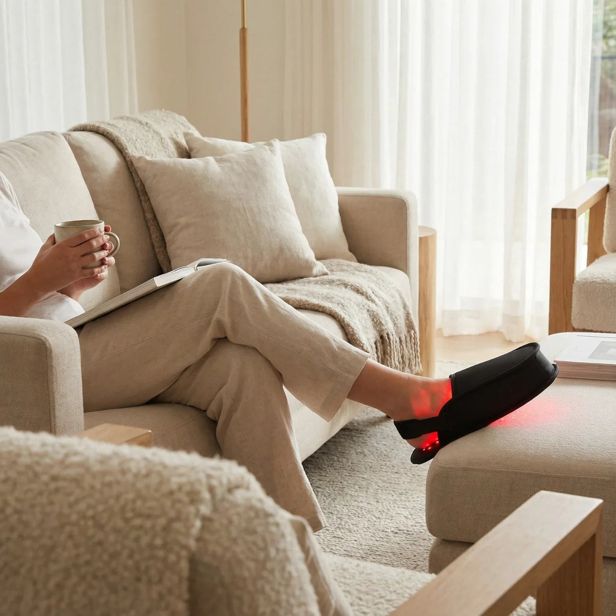 Black red light therapy slippers worn on feet while seated on a sofa