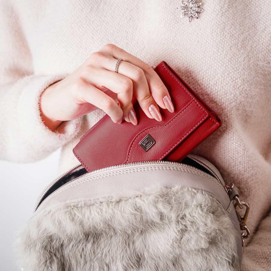 Red leather wallet with snap front and metal emblem held over a bag