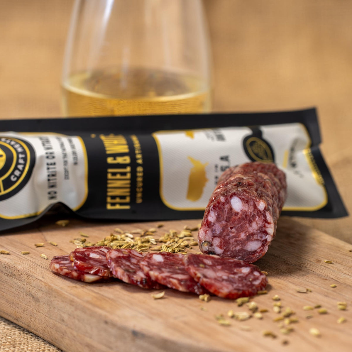 Fennel & white wine salami log with slices and herbs on a wooden board
