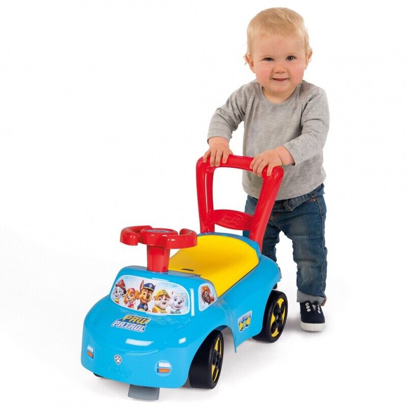 Blue Paw Patrol ride-on pusher car with red handle and yellow seat, child standing behind.