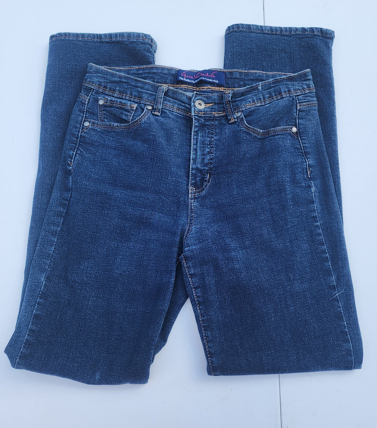 Women's blue jeans laid flat, medium wash denim with belt loops and button closure