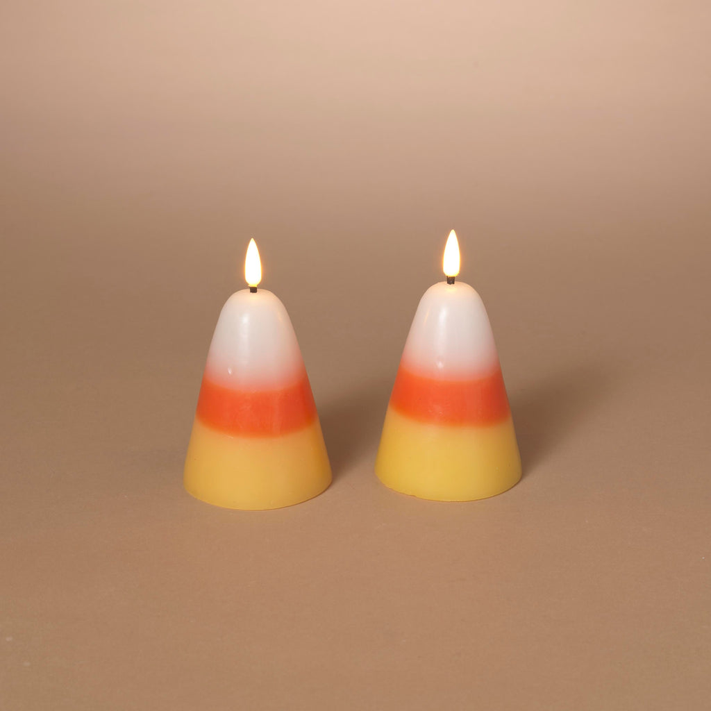 Two small lit candy corn wax candles with white, orange, and yellow layers