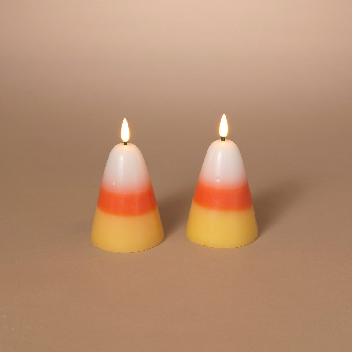 Two small lit candy corn wax candles with white, orange, and yellow layers