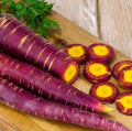Purple heirloom carrots with bright yellow-orange centers, sliced and whole on board