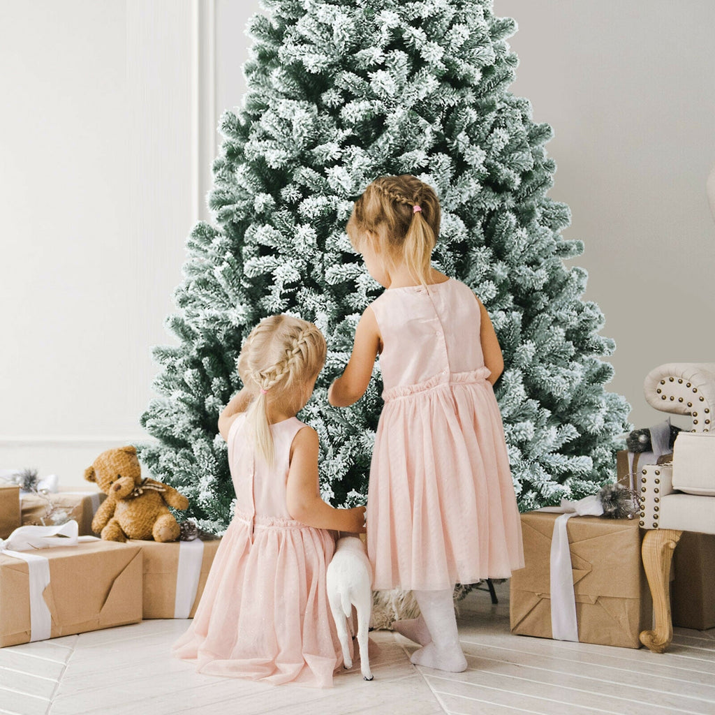 Snow flocked Christmas tree with dense branches, viewed from behind with children nearby