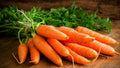 Orange carrot roots with green tops, bundled on a wooden surface