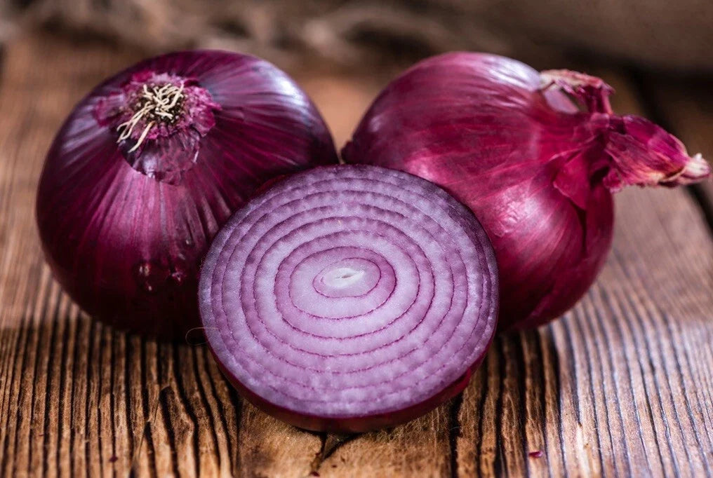 Red creole onion bulbs with sliced interior on wooden surface