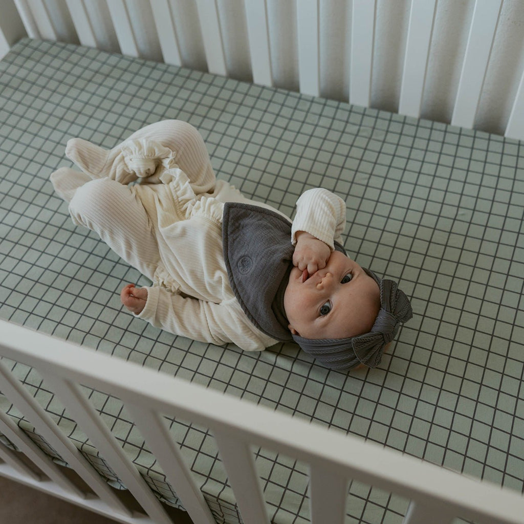 Crib sheet in off-white with light green grid pattern, laid across a crib